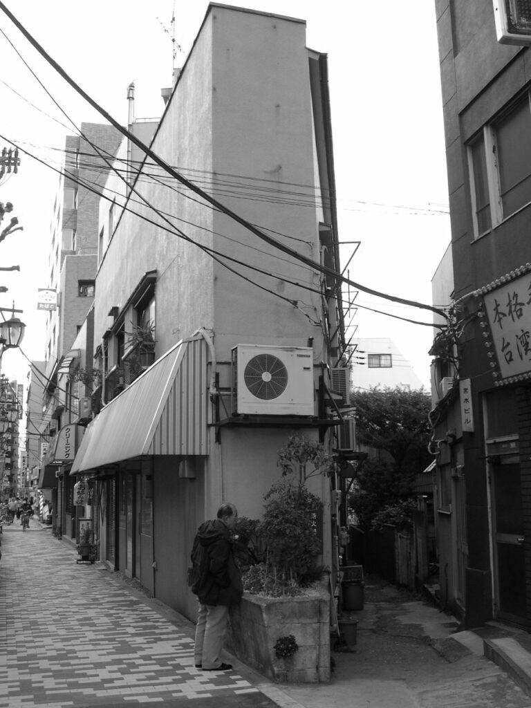 Homme observant une plante devant un bâtiment très étroit au Japon.