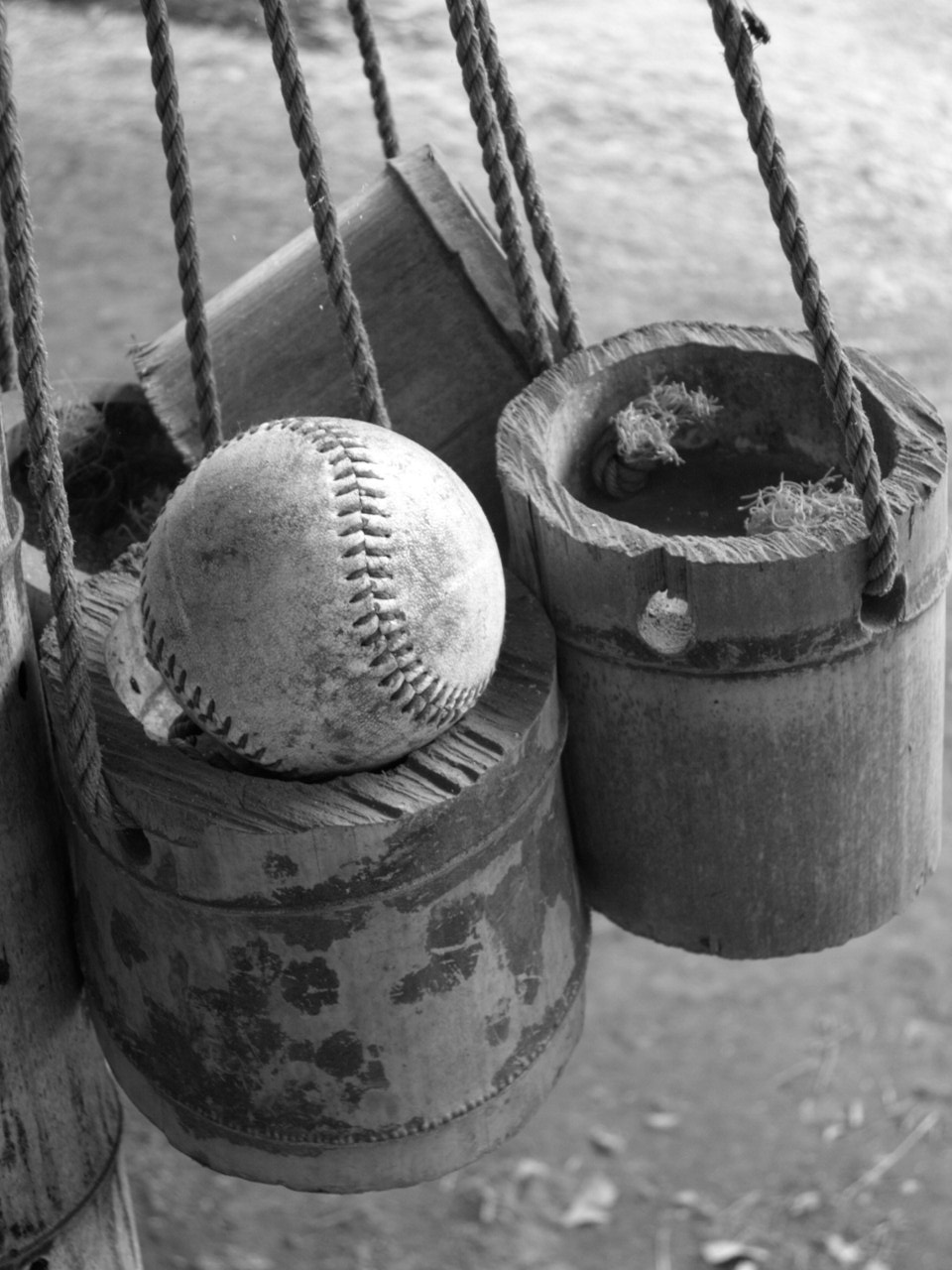 Balle de baseball usée posée dans un vieux seau en bois suspendu par des cordes.