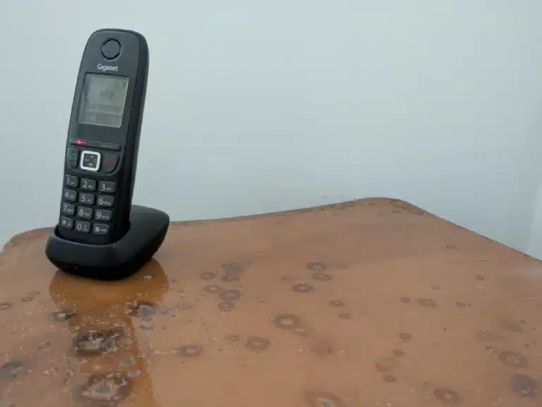 Un téléphone, seul sur une tablette. Derrière, un mur blanc.