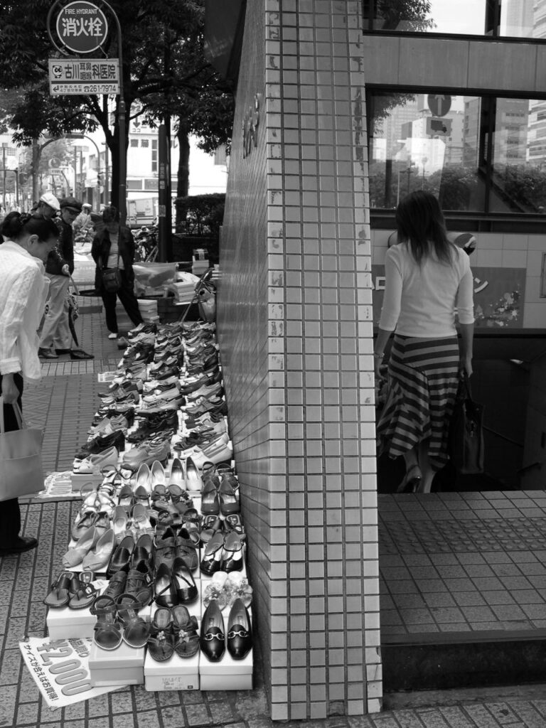 Scène urbaine au Japon avec des femmes devant un étal de chaussures et une femme descendant les escaliers d'une station de métro.