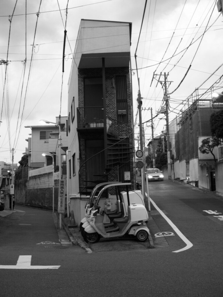 Habitation très étroite coincée entre deux rues au Japon, sous un dense réseau de lignes électriques.