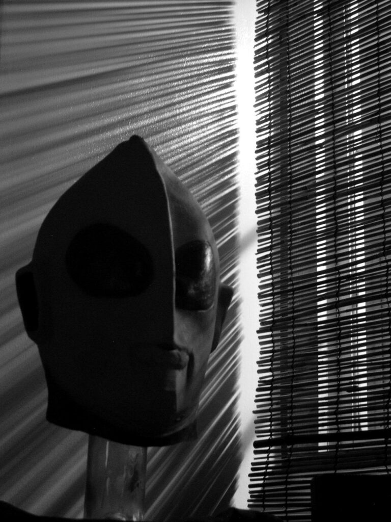 Un masque d'Ultraman se détache dans les rayons de lumière filtrant à travers une persienne.