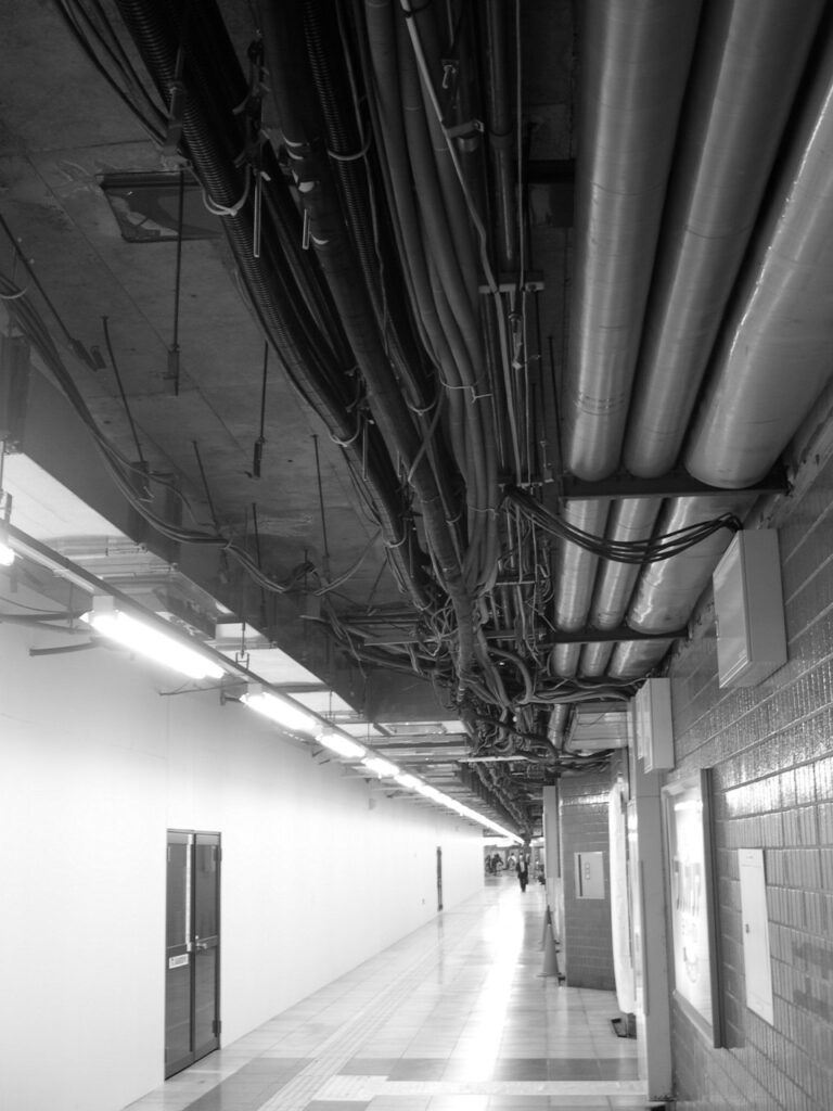 Long couloir de métro au Japon, où la tuyauterie et le réseau de câbles sont apparents.