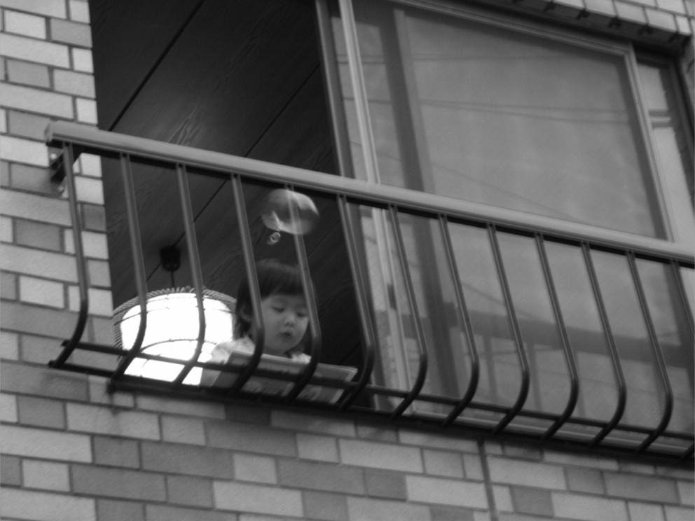 Petite fille appuyée au balcon d'un appartement japonais, avec une bulle s'élevant au-dessus d'elle.